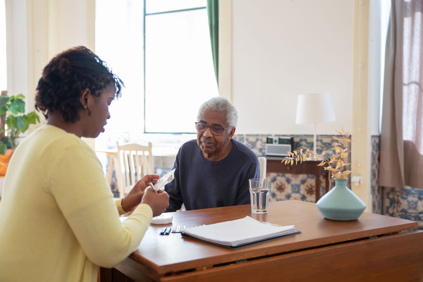A care worker supporting an older adult with medication at a table